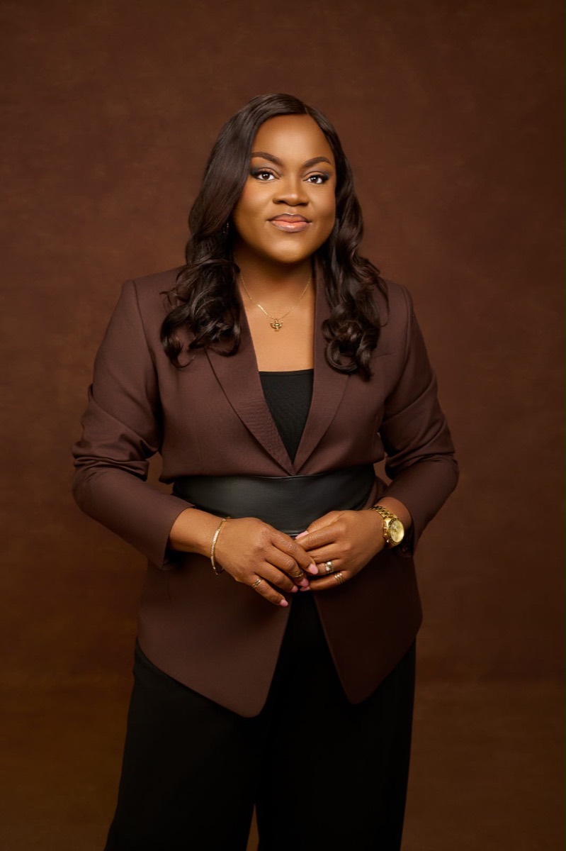 Busayo Disu standing in a brown blazer, hands gently clasped