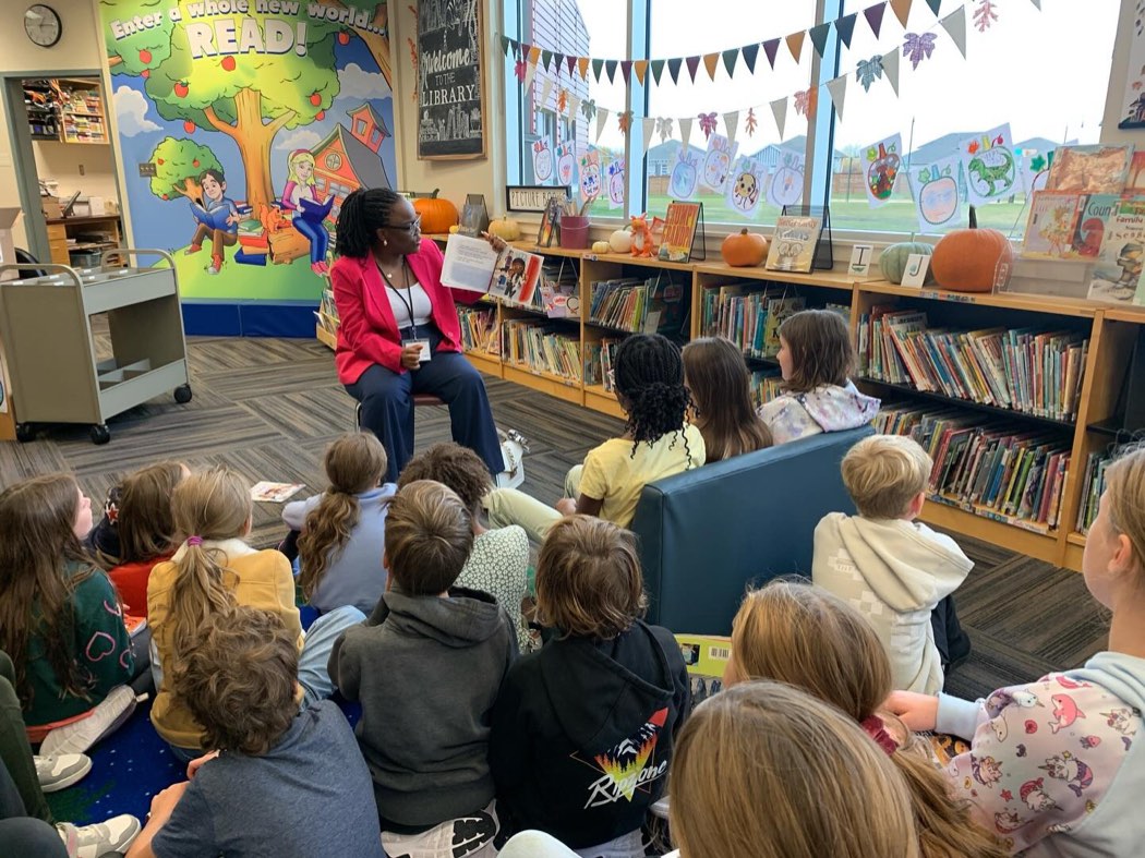Busayo Disu, as Mrs. Disu, reading a picture book aloud to children at story time in a school library