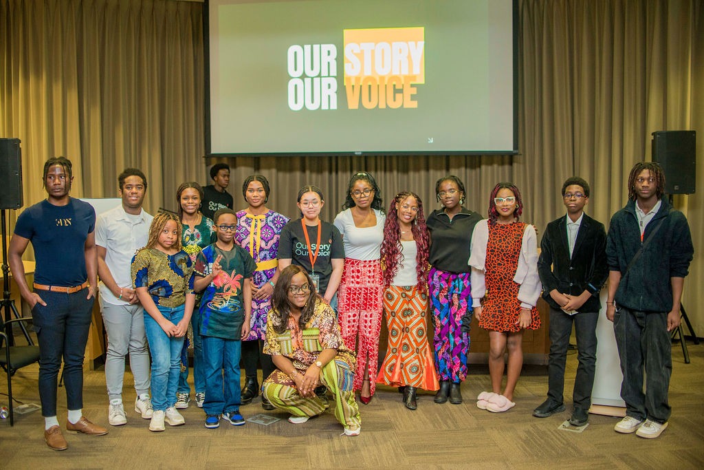 The young people of Our Story, Our Voice with Busayo Disu, standing under the collection&rsquo;s title on the screen behind them
