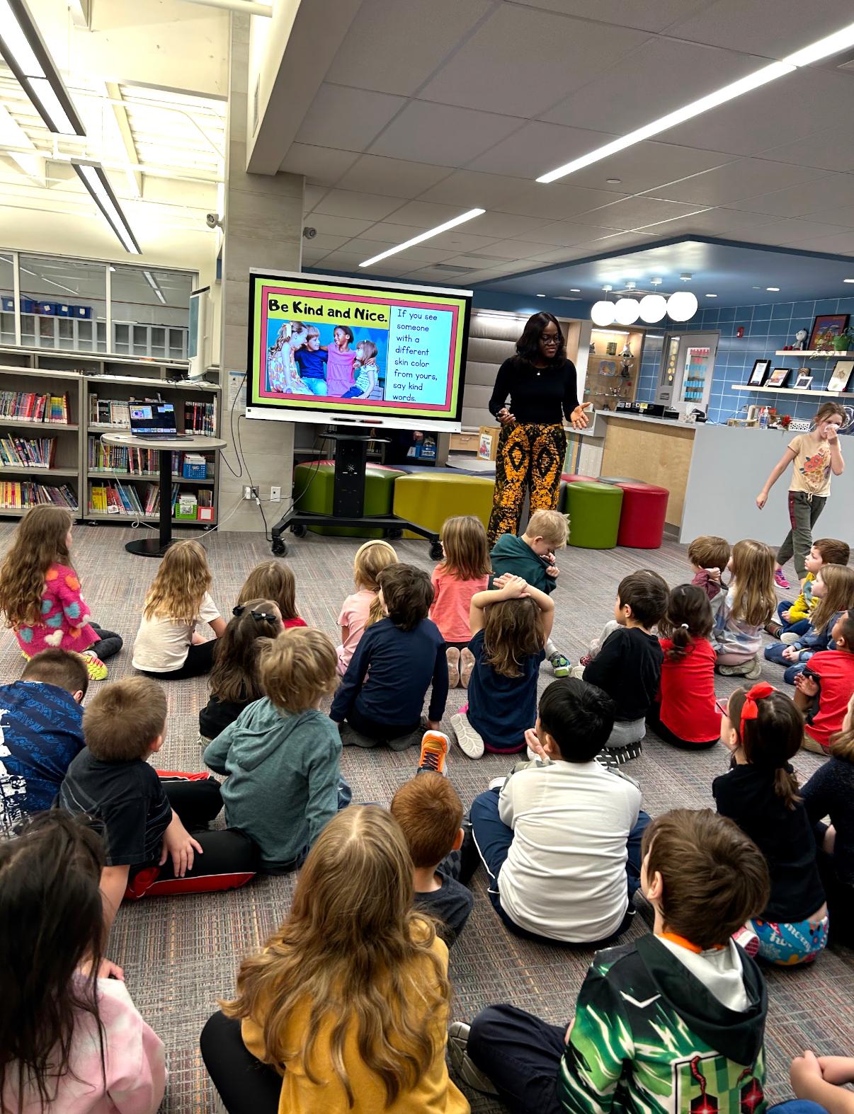 Children sitting on a school library floor in front of Busayo Disu&rsquo;s &ldquo;Be Kind and Nice&rdquo; slide