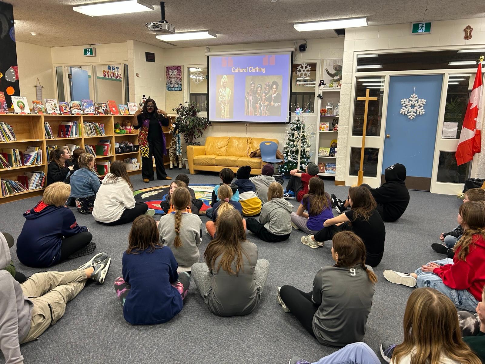 Busayo Disu talking about cultural clothing to children sitting on a school library floor